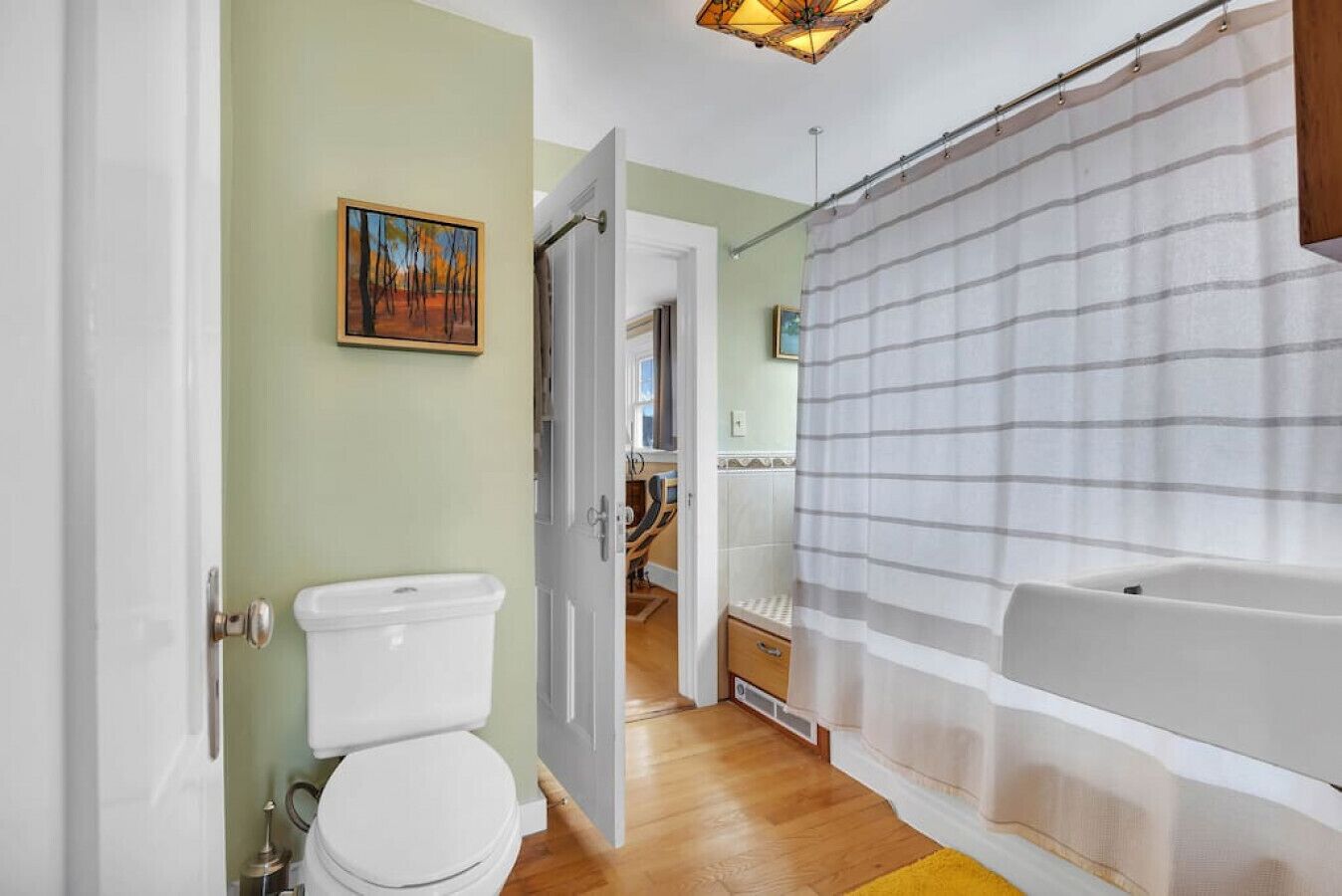Een badkamer met toilet, douchegordijn en houten vloer.