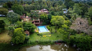 A residential area with a swimming pool, a boat on the water, and lush greenery. - Ayurveda Spring of life Resort (Piliyandala)
