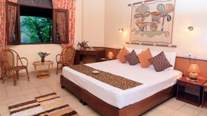 A neatly arranged bedroom with a large bed, two bedside tables, a small table with a vase, and wicker chairs. - Ayurveda Spring of life Resort (Piliyandala)