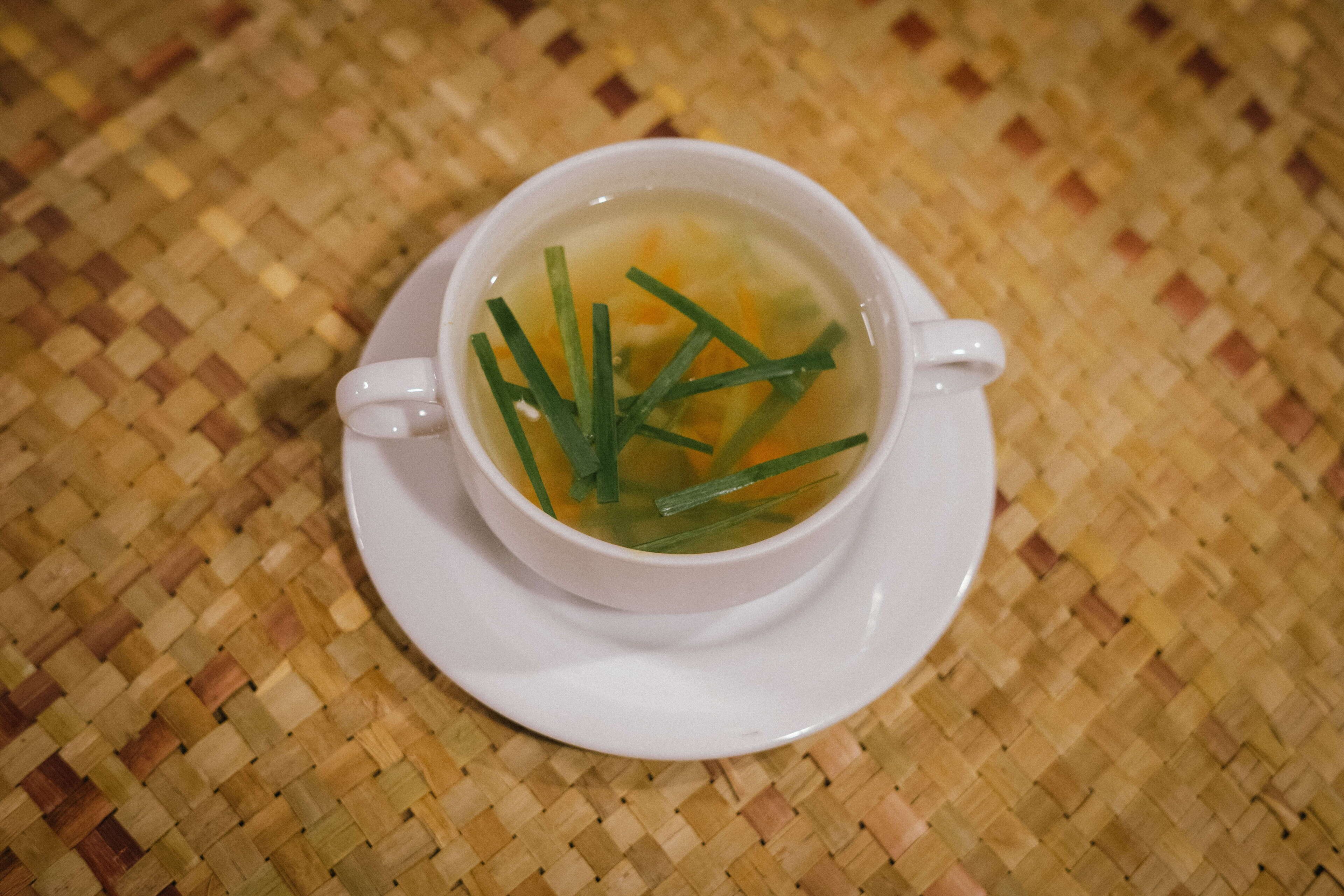 A white cup of soup with green garnish on a woven mat.