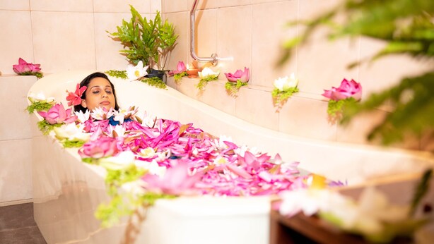 A bathtub filled with pink and white flowers, surrounded by potted plants and candles. - Ayurveda Spring of life Resort (Piliyandala)