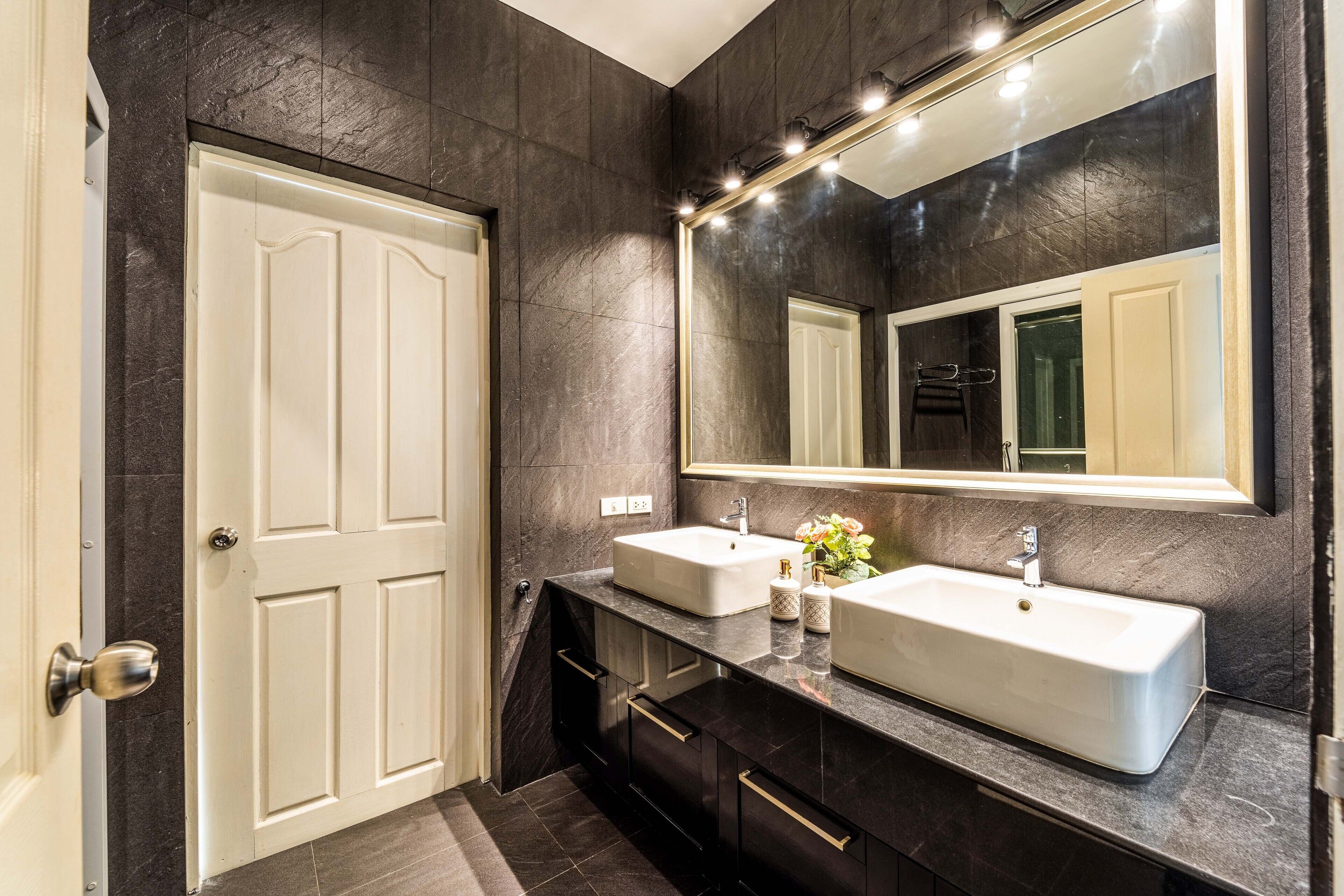 A modern bathroom with two sinks, dark stone walls, and a large mirror.