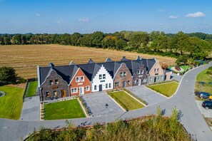 A row of traditional European-style houses with sloped roofs, a central courtyard, and a surrounding green landscape. - Vacation home "Wangerooge" with 102 sqm - in the vacation park Harkebrügge (Barßel)