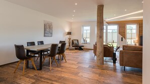 Une pièce spacieuse avec un plancher en bois, une table à manger avec des chaises, un canapé et une grande fenêtre.