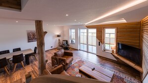 Un vaste salon doté d’un plancher en bois, d’un grand téléviseur fixé au mur et d’un coin repas avec une table et des chaises.