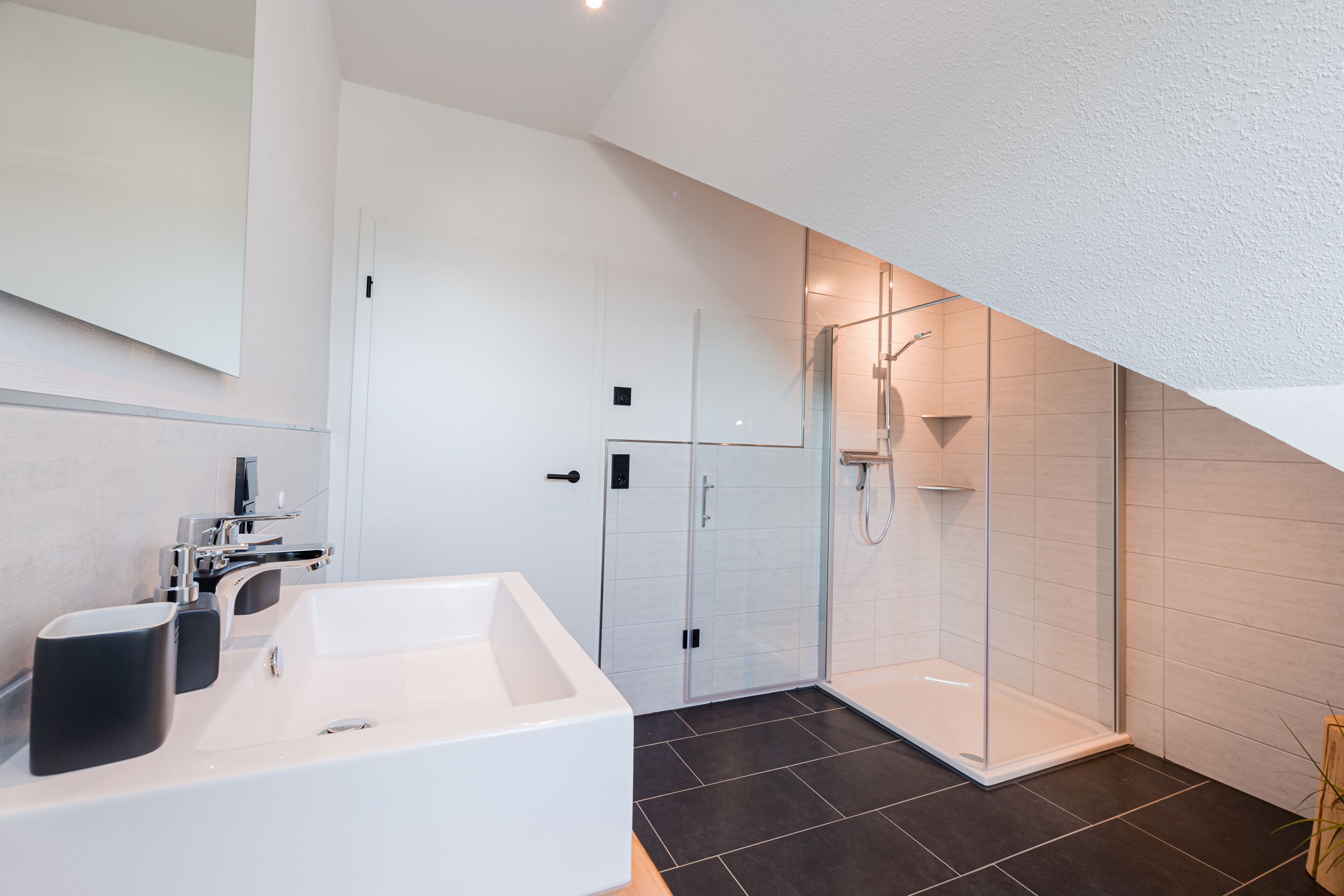 A modern bathroom with a large white bathtub, a glass-enclosed shower, and dark tiled flooring.