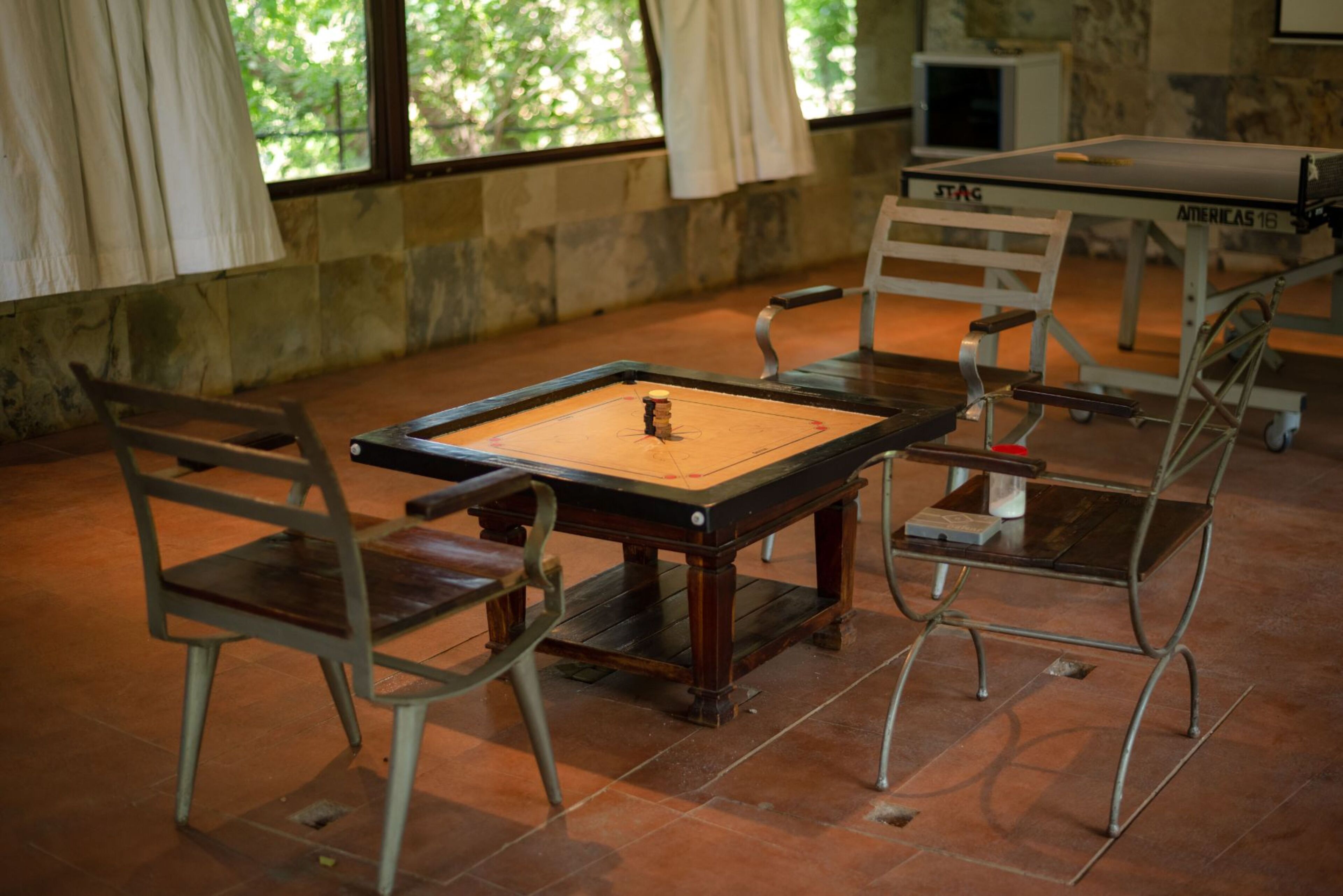 Una mesa de ping pong con sillas, una pared de piedra y una ventana con cortinas.