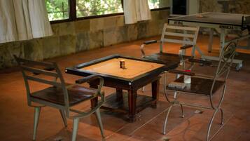Una mesa de ping pong con sillas, una pared de piedra y una ventana con cortinas.