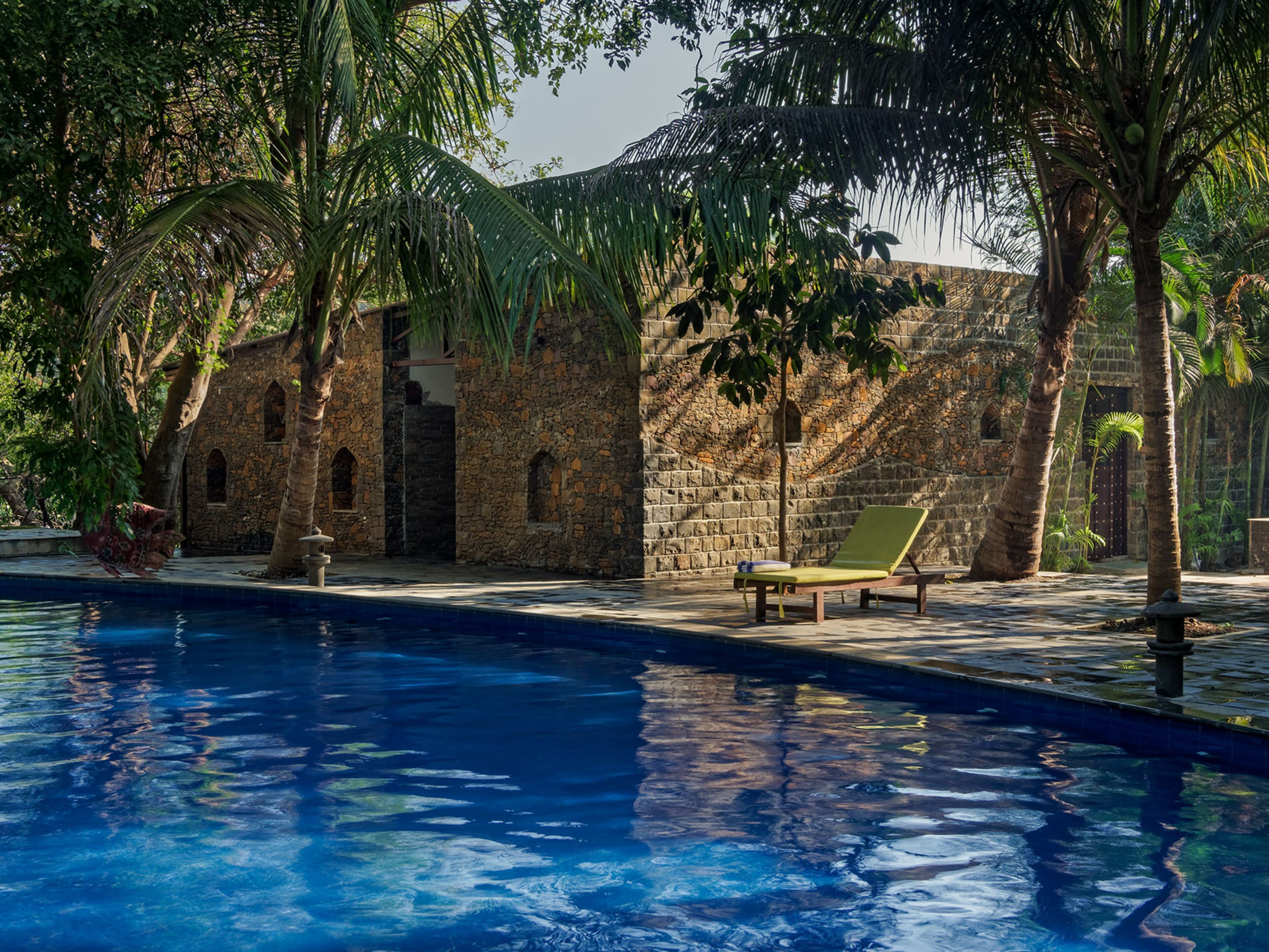 A pool area with a stone building, palm trees, and a lounge chair.