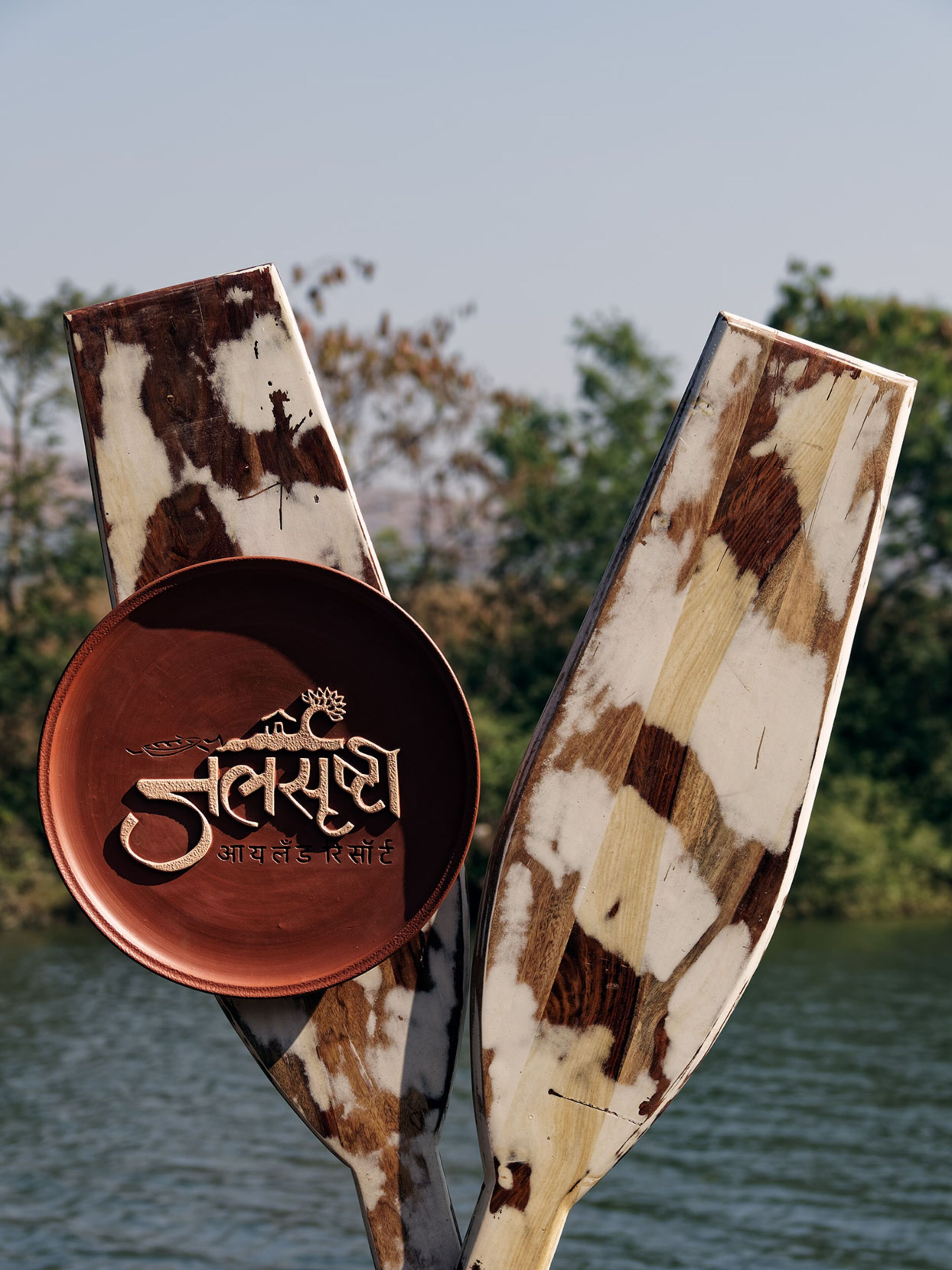 A wooden boat with a metal plate engraved with text, set against a body of water with trees in the background.
