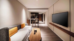 A modern hotel room with a sofa, a coffee table, a flat-screen TV mounted on the wall, and a kitchen area in the background. - UrCove by Hyatt Shanghai Lujiazui EXPO (Shanghai)