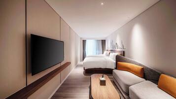 A modern hotel room with a flat-screen TV mounted on the wall, a sofa, a bed, and a small wooden table.