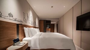 A modern hotel room with a large bed, a bedside table with a laptop, a wall-mounted TV, and a decorative wall mural. - UrCove by Hyatt Shanghai Lujiazui EXPO (Shanghai)