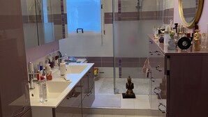 A modern bathroom with a glass shower enclosure, a large mirror, and a chandelier. - Champs Élysées (Paris)