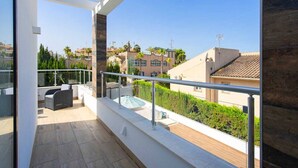Un balcone con ringhiera in vetro, arredi da esterno e vista sugli edifici circostanti.