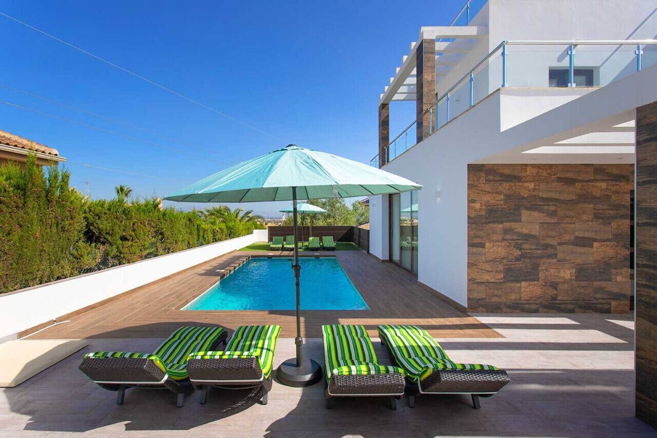 Ein moderner Poolbereich im Freien mit Liegestühlen und einem großen Sonnenschirm.