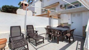 A patio area with a table and chairs, a small seating area with a chair and a stool, and a white building in the background.