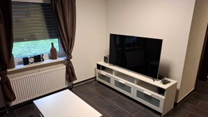 Ein modernes Wohnzimmer mit Flachbildfernseher, einem weißen Couchtisch und einem Fenster mit Vorhängen.