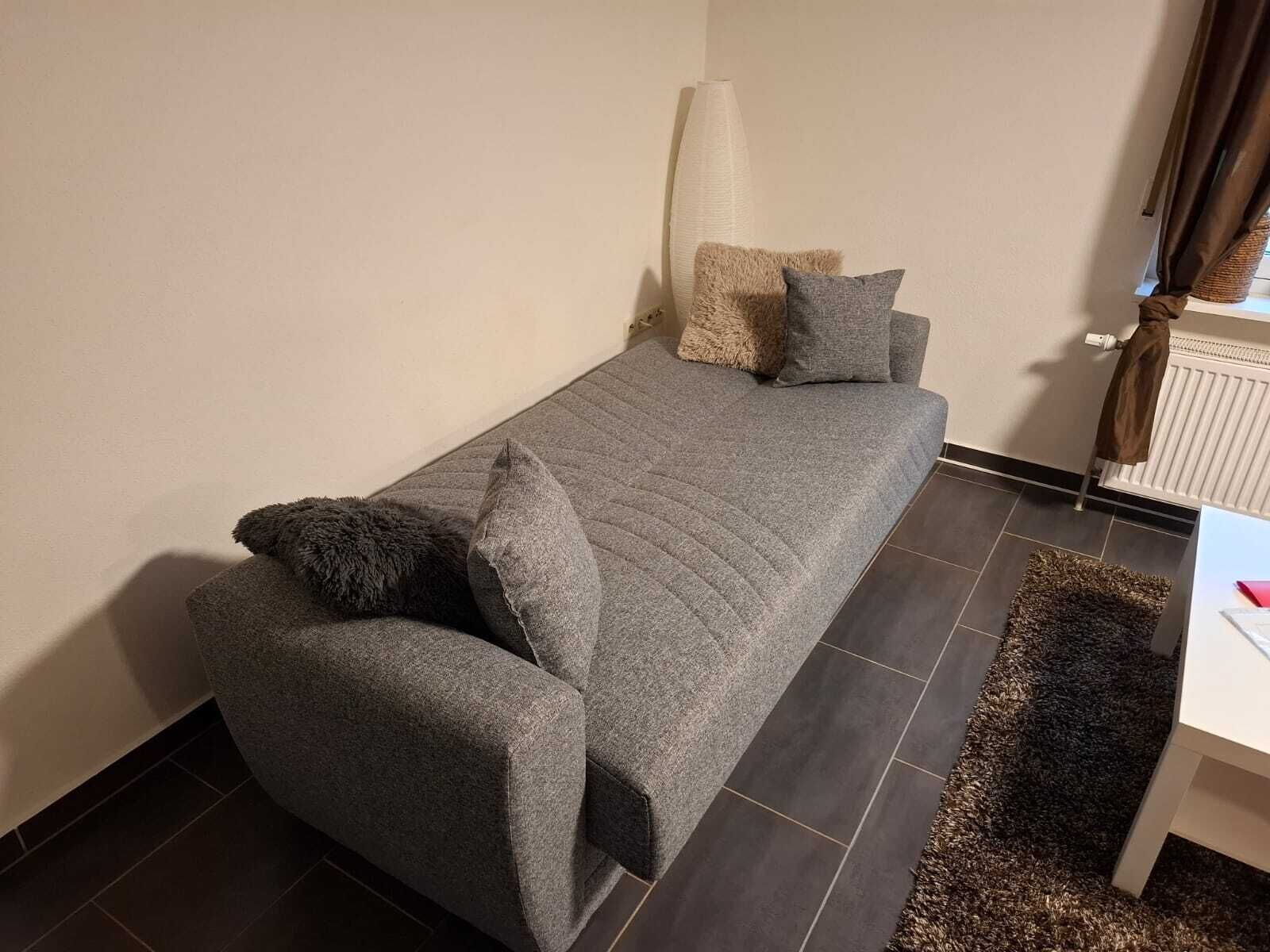A small, neatly arranged bedroom with a single bed, a bedside table, and a radiator.