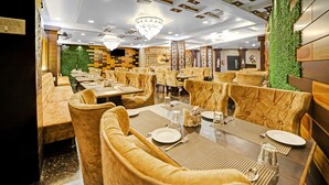 A restaurant with velvet chairs, wooden tables, and a green wall. - The Bagga Inn (Jabalpur)