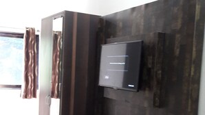 A modern living room with a built-in entertainment unit, a flat-screen TV, and a small cabinet. - The Bagga Inn (Jabalpur)