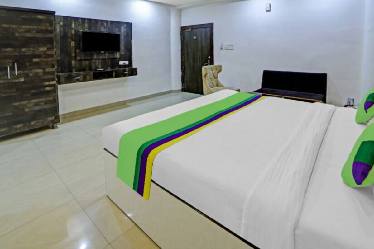 A hotel room with a large bed, a TV mounted on the wall, a wardrobe, and a desk with a chair.