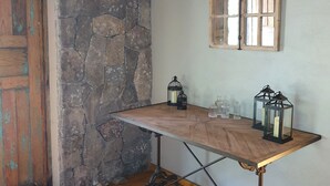 Quarto rústico com parede de pedra, porta de madeira e uma mesa com lanternas.