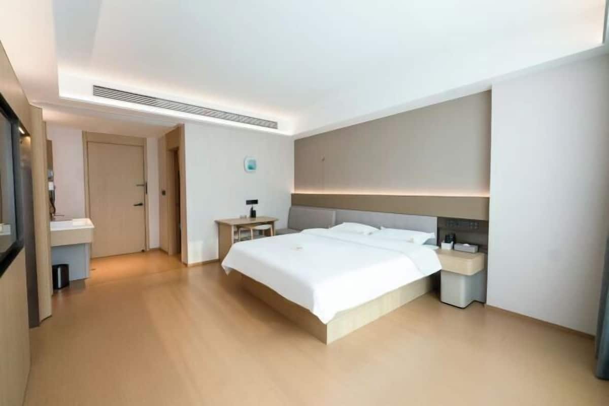 A modern hotel room with a large bed, bedside tables, a nightstand, and a built-in bench.