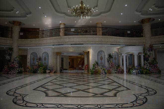 A grand lobby with a large marble floor, a chandelier, and a balcony with railings.