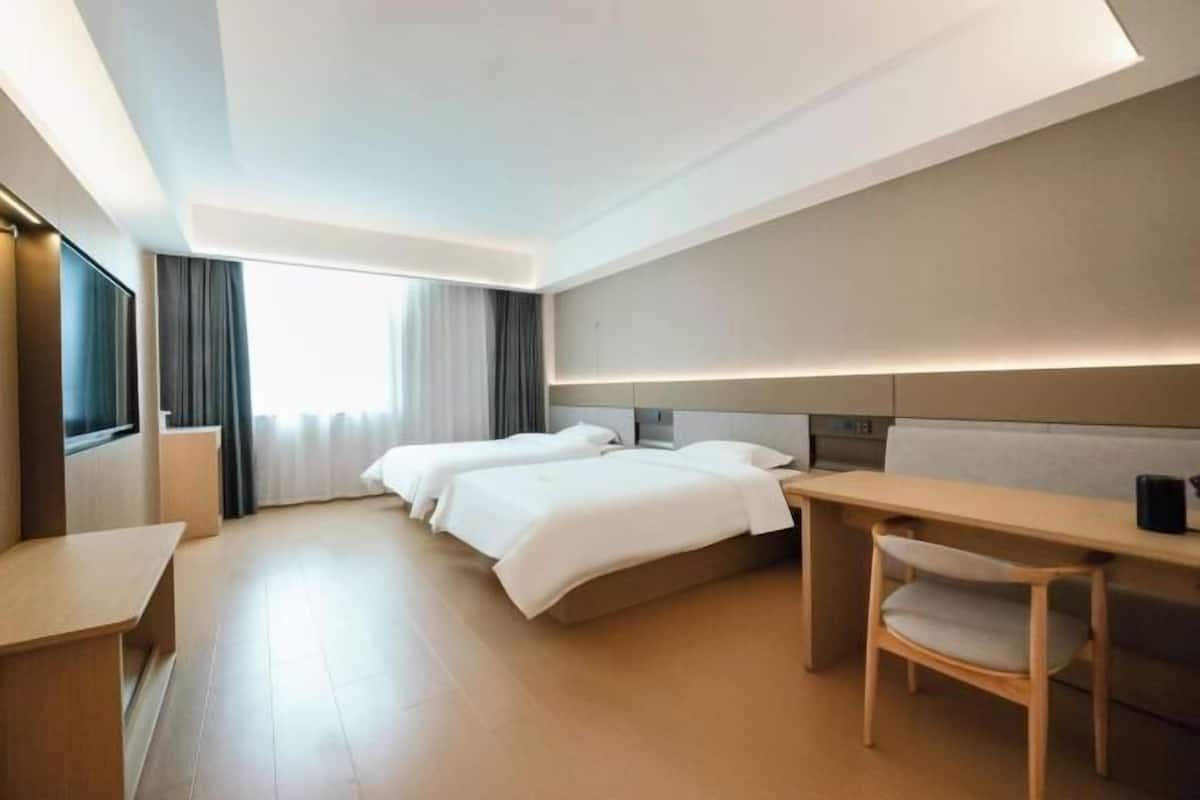 A hotel room with two beds, a desk, a chair, and a large window with curtains.
