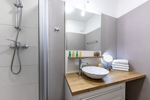 A bathroom with a shower, a sink, a mirror, and a towel rack.