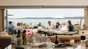Un grupo de personas cenando en una mesa al aire libre con vistas al mar.