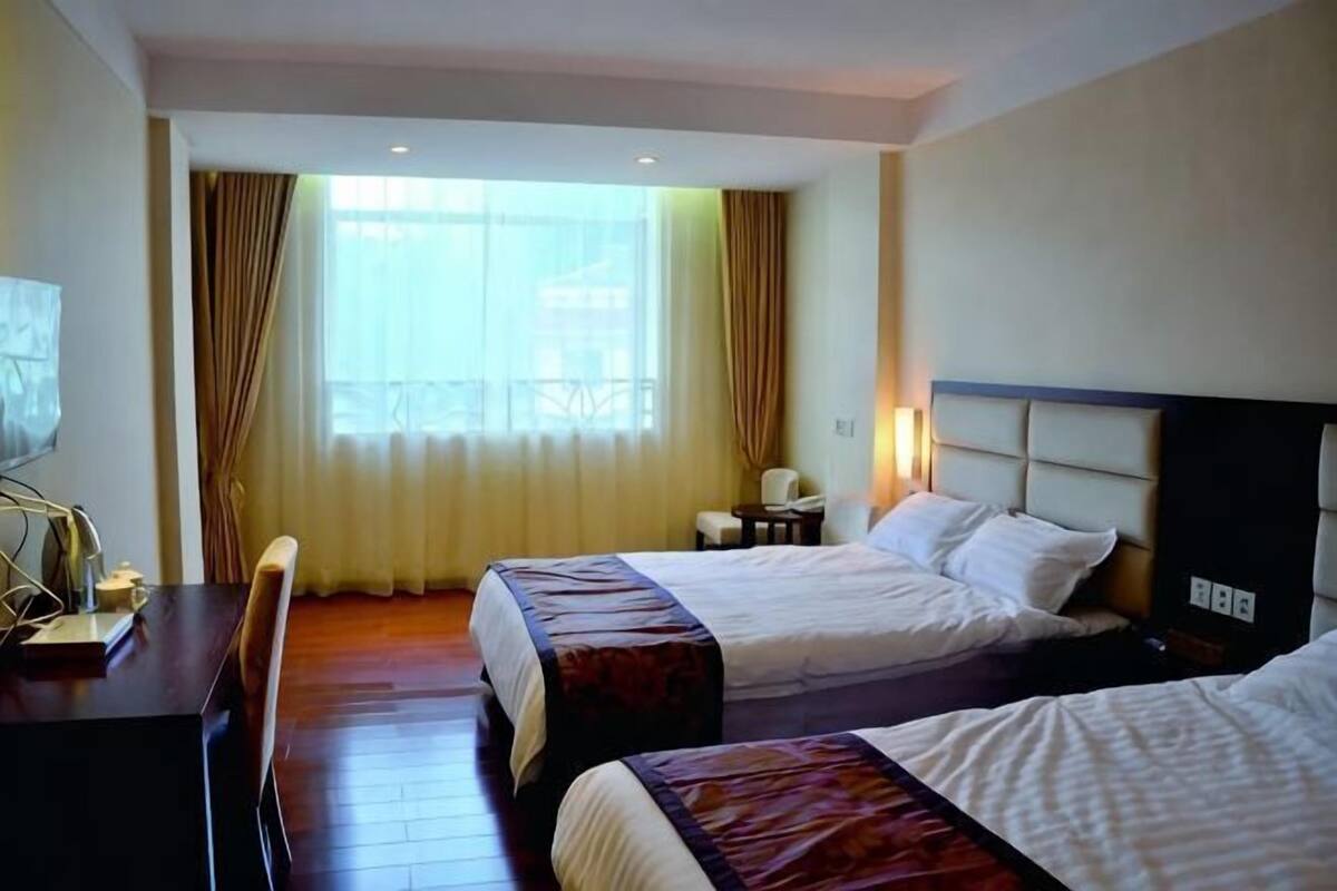 A hotel room with two beds, a desk, a chair, a TV, and a window with curtains.