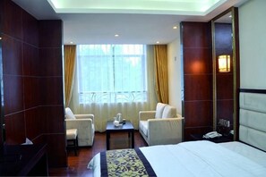 A hotel room with a bed, two chairs, a small table, a nightstand, and a window with curtains. - Fenggang Furongxin Hotel (Fenggang)