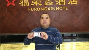 A man holding a hotel card in front of a sign with the name 'Fulongxin Hotel'. - Fenggang Furongxin Hotel (Fenggang)