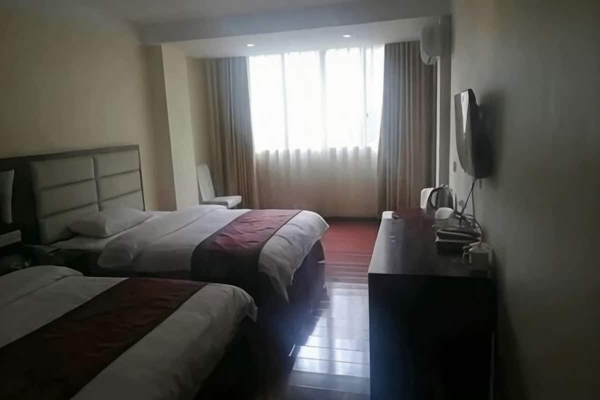 A hotel room with two beds, a desk, a chair, a TV, and a window with curtains.