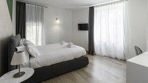 A modern hotel room with a large bed, a bedside table with a lamp, a flat-screen TV mounted on the wall, and a large window with sheer curtains. - Italianway Collection - Corso Como 11 - D (Milan)