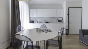 A modern kitchen with white cabinets, a microwave, and a coffee maker. There is a dining table with chairs and a grey sofa in the living area. - Italianway Collection - Corso Como 11 - D (Milan)