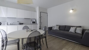 A modern living room with a dark grey sofa, a round dining table with chairs, and a kitchen area with white cabinets and a microwave. - Italianway Collection - Corso Como 11 - D (Milan)