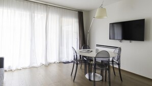 Ett modernt matområde med ett runt bord, genomskinliga stolar, en golvlampa och en platt-TV som är monterad på väggen.