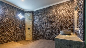 Ein Badezimmer mit Steinwänden, einer Dusche, einem großen Waschbecken und einem Dachfenster.