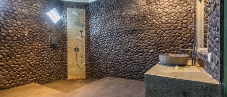 Un baño con paredes de piedra, ducha, un lavamanos grande y un tragaluz.