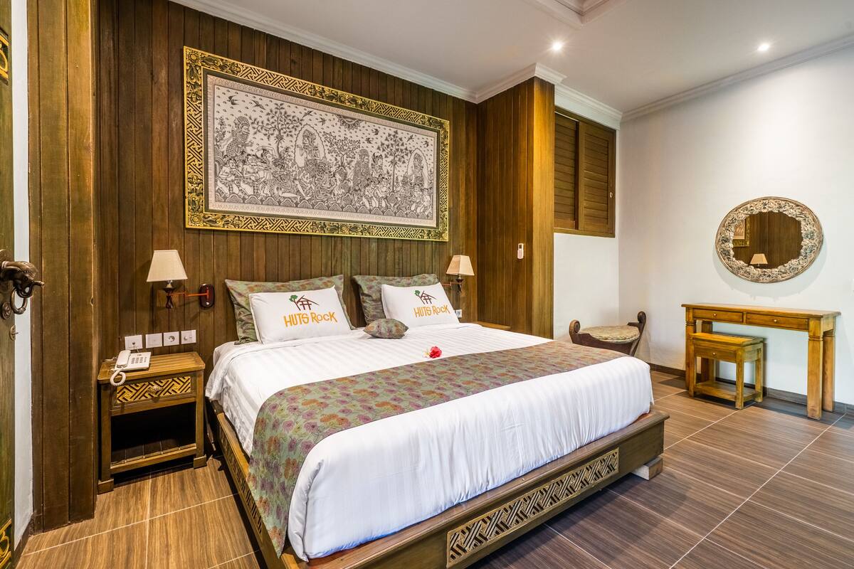 A spacious bedroom with a large bed, wooden paneling, a decorative wall hanging, and a small wooden desk.