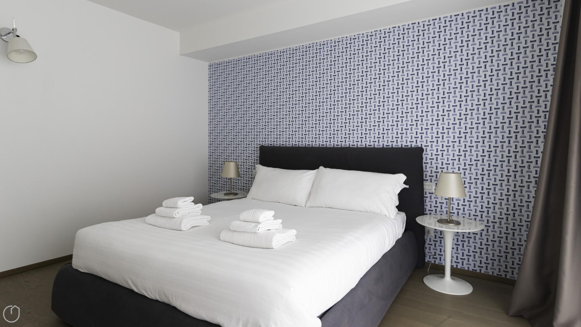 A hotel room with a neatly made bed, two bedside tables with lamps, and a patterned wall.