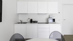 A modern kitchen with white cabinets, a sink, a microwave, and a coffee maker. There is a dining table with chairs in front.