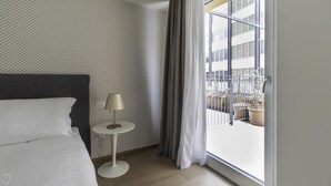 A hotel room with a bed, a small table with a lamp, a window with curtains, and a view of the cityscape. - Italianway - Corso Como 11 - 7 (Milan)