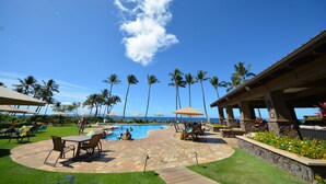 A pool area with lounge chairs, umbrellas, and palm trees. - Ekahi 27A: Priceless Ocean View from a Private Lanai (Kihei)