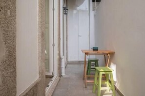 Un couloir étroit avec une table en bois et deux tabourets verts.