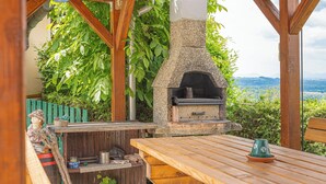 An outdoor patio with a stone-built pizza oven, wooden tables, and a rustic bench. - Vineyard Cottage Vesna Lake View (Cirkulane)
