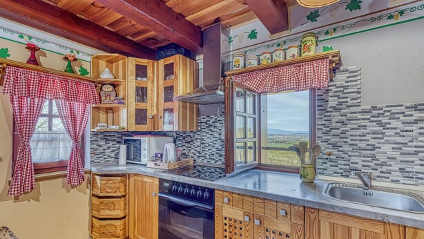 A kitchen with wooden cabinets, a stove, and a window with a view. - Vineyard Cottage Vesna Lake View (Cirkulane)